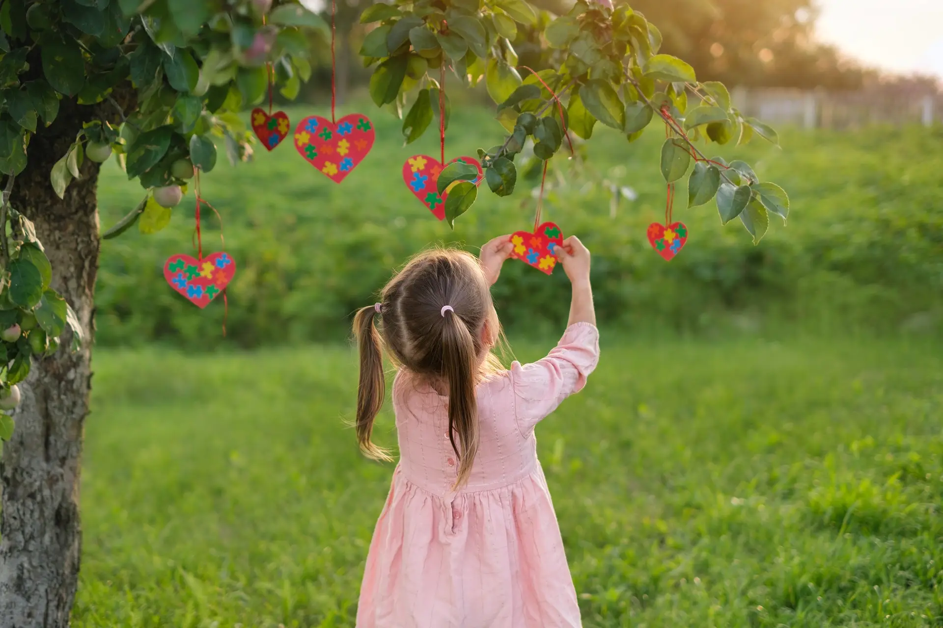 Kid decorates branches with hearts cards with multicolored puzzle on autism day